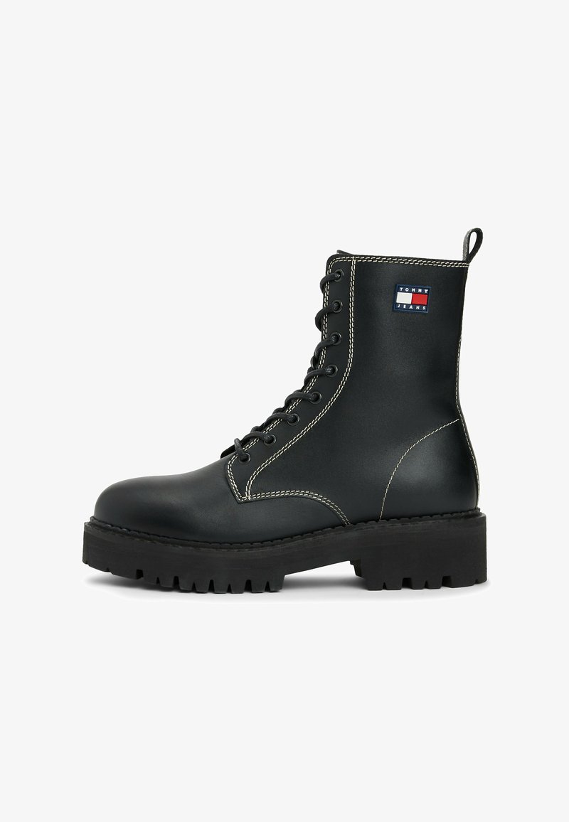 Stivale in pelle nera con lacci, suola spessa, cuciture bianche, linguetta di inserimento e patch con il logo Tommy Jeans sul lato.
