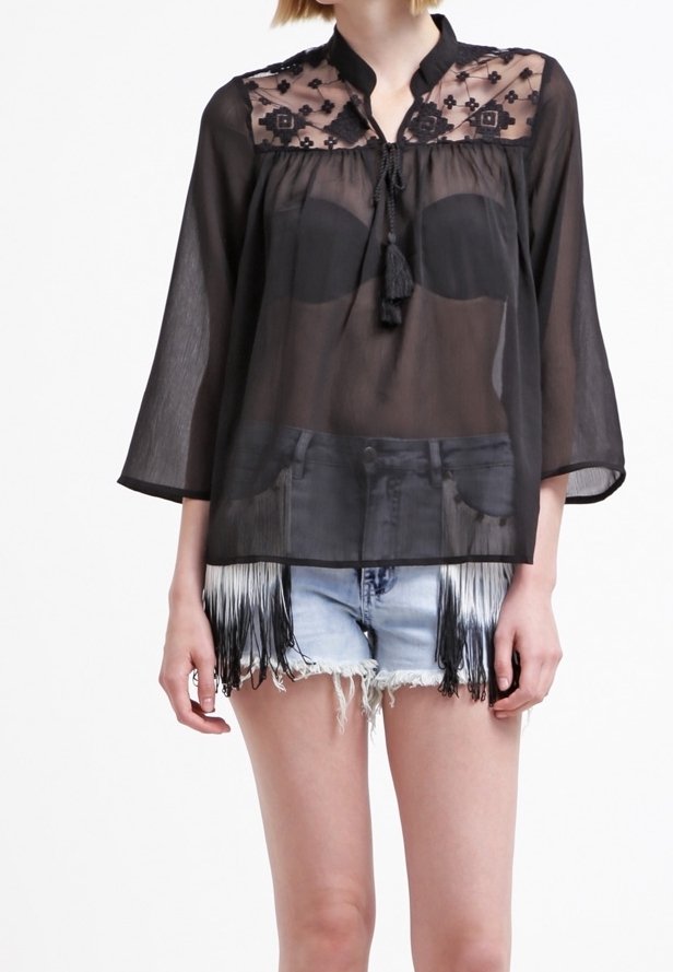 Zwarte transparante blouse met geborduurde kant yoke, mandarin kraag en 3/4 mouwen. Gecombineerd met versleten denim shorts met franjes.