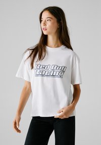 T-shirt en coton blanc avec un imprimé bleu "Red Bull Racing" sur la poitrine, à manches courtes et avec une coupe décontractée.