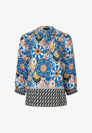 Bunt gemusterte Bluse mit floralen Motiven in Blau, Orange und Schwarz, mit Dreiviertelärmeln und einem schwarzen geometrischen Band am Saum.
