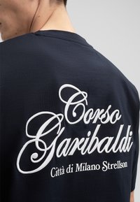 Navyblauwe T-shirt met witte geborduurde tekst die zegt "Corso Garibaldi Città di Milano Strellson", met een soepele, zachte textuur.