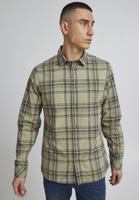 Beige og sort ternet langærmet skjorte med knapkrave og to foranliggende lommer, lavet af struktureret stof.