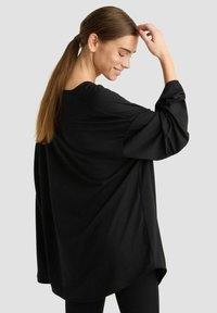 Schwarzes, oversized Langarmhemd mit abgerundetem Saum und lockerem Schnitt, aus weichem Stoff gefertigt. Es verfügt über einen weiten Halsausschnitt und überschnittene Schultern.