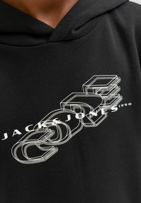 Felpa nera con cappuccio caratterizzata da una stampa grafica bianca con il testo "JACK & JONES 1990" e un design stilizzato di lettere e forme sovrapposte.