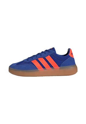 Blauer Sneaker mit orangen Streifen und Fersenlasche, Schnürdesign und dicker durchsichtiger brauner Sohle, Seitenansicht.