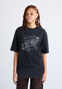 Tricou negru supradimensionat cu o textură uzată, având un design grafic central cu text gri. Asortat cu pantaloni din catifea ribbed maro.