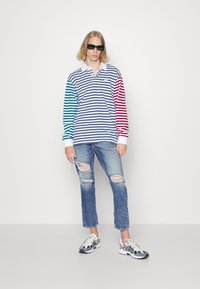 Langermet stripete polo-skjorte med blå, teal og røde ermer, brukt med slitte blå jeans og svart-hvite joggesko.