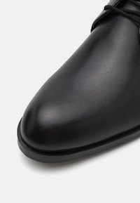 Černá kožená bota s hladkým povrchem, špičatou špičkou a minimalistickým designem. Vybavena tenkou černou gumovou podrážkou pro trvanlivost.