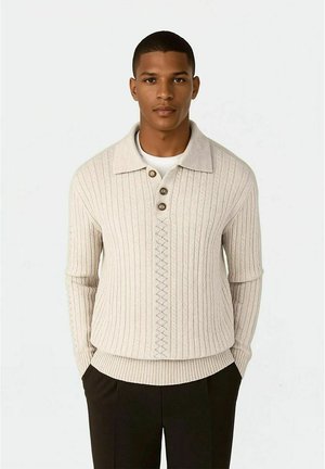 Lys beige strikket genser med krage, tre knapper, ribbestrikket tekstur og diamantmønster foran.
