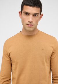 Langärmliges T-Shirt mit Rundhalsausschnitt in einem hellbraunen Farbton, aus weicher Baumwolle gefertigt, mit einem dezenten, auf der Brust gestickten Logo.