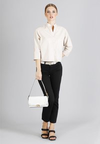 Beige beskåret skjorte med knapper og stående krave, sorte slim-fit jeans, hvid håndtaske med rynket design og sorte platform sandaler.