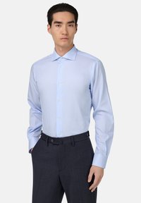 Lichtblauw gestreept overhemd van gladde stof; heeft een klassieke kraag, knopen aan de voorkant en lange mouwen, gecombineerd met donkere broeken.