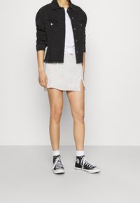 Veste en denim noir avec des boutons à l'avant et ourlet effiloché, t-shirt blanc, mini-jupe à motif floral avec fente sur le côté, et baskets montantes noires.