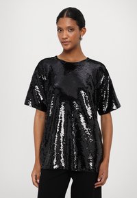 Black sequin top with short sleeves, round neckline, and a loose fit. The fabric is shiny with a textured surface, reflecting light.