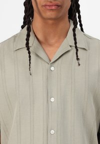 Light green button-up shirt with vertical stripe pattern, short sleeves, and a collar. Features white buttons and soft, textured fabric.