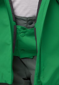Zelená voděodolná bunda se šedým podšívkou, s patentním zapínáním a zipovými kapsami, která ukazuje hladkou texturu látky.