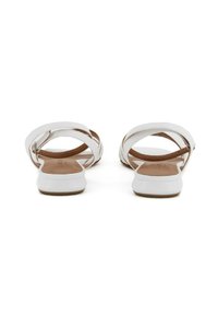 Sandali bianchi con design a cinghie incrociate, texture liscia e suola piatta. Presentano una soletta marrone chiaro e un aspetto minimalista.