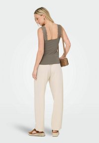 Grå tanktop med blonderemmer, parret med lysebeige vide bukser og brune espadrille-sandaler. Modellen bærer en lille brun taske.