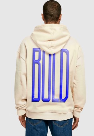 Beige oversized hoodie med dobbeltforet hætte. Har stort blåt "BOLD" tekst på ryggen. Fremstillet af blødt, struktureret stof.