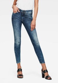 Skinny jeans in donkerblauwe denim, met een middelhoge taille, subtiele vervaging en een zachte textuur. Gepaard met zwarte blokhak sandalen.