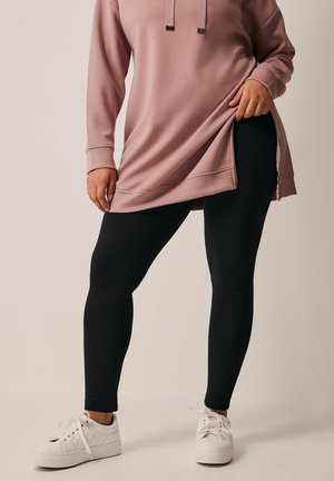 Mustat legginsit yhdistettynä vaaleanpunaiseen ylisuurta huppariin, jossa on sivuaukot ja säädettävät nyörit. Valkoiset tennarit viimeistelevät asun.