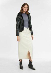 Zwarte leren motorjack, grijs aansluitend top, crèmekleurige midi-rok met een split aan de voorkant, en zwarte gestructureerde enkellaarsjes met een blokhak.