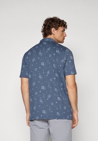 Blå polo med korte ermer som har et strukturert mønster med forskjellige former og design i lysere nyanser. Har krage og en avslappet passform.