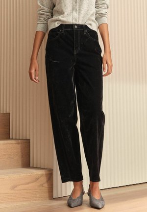 Schwarze Cordhosen mit hoher Taille, geradem Bein und subtiler Textur, kombiniert mit einer hellgrauen, geknöpften Strickjacke und funkelnden Schuhen.
