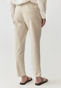 Pantalones beige a rayas con un corte ajustado, que incluyen un diseño de bolsillo trasero y una tela suave y texturizada. Completados con sandalias planas.