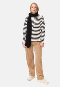 Gestreepte zwart-witte longsleeve shirt met knopen, gecombineerd met tan corduroy broek en een zwarte sjaal, gedragen met witte sneakers.
