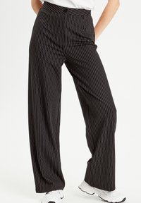 Pantalons larges à rayures noires avec une taille haute et une poche devant, présentant des rayures blanches et une texture lisse.