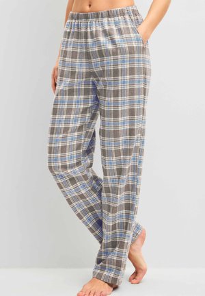 Femme portant un pantalon de pyjama ample à carreaux gris, bleu et blanc avec une taille élastique, debout pieds nus avec une main dans la poche.