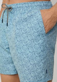 Pantaloni da bagno azzurri chiari con motivo a foglie, fascia elastica in vita e cordoncino. Presentano tasche laterali e un'etichetta con logo sull'orlo.