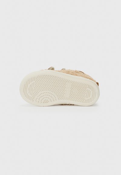 Lys beige kunstpels slip-on sko med en teksturert kremfarget gummisåle, med zigzag-mønster og subtile stitch-detaljer.