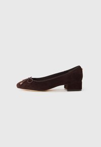 Dark brown suede low-heeled ballet flat with rounded toe and small bow on light neutral background.