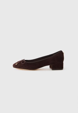 Dark brown suede low-heeled ballet flat with rounded toe and small bow on light neutral background.