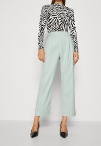 Zwart-wit zebra print lange mouwen top gecombineerd met licht muntgroene wijde broek en zwarte puntige hakken.