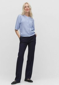 Ljusblå kortärmad cardigan med strukturmönster och pärlknappar, tillsammans med svarta skräddarsydda byxor och platta skor.