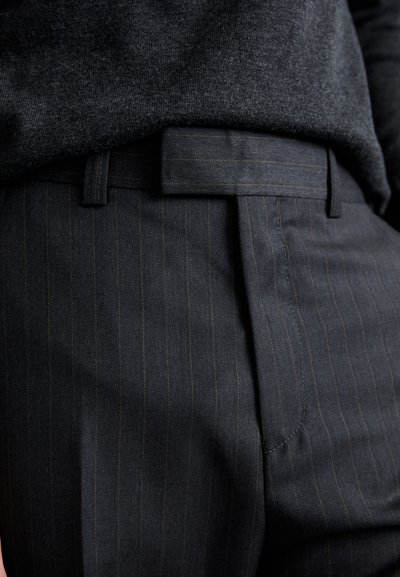 Sorte pinstribede bukser med en glat tekstur, der har flad front, bæltestropper og minimale syninger. Fremstillet af holdbart stof.