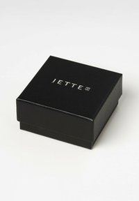 Scatola per gioielli nera, con texture e coperchio a cerniera. Presenta la scritta argentata "JETTE" sulla parte superiore. Design compatto quadrato, bordi lisci.