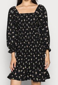 Czarna sukienka z marszczeniami i długimi bufiastymi rękawami, w kwiatowy wzór w odcieniach niebieskiego, zielonego i różowego, z falbaniastym dołem.