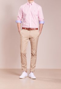 Ljusrosa skjorta med knappar och blå manschetter, beige chinos, brun bältesrem och vita sneakers. Avslappnad passform, mjukt tyg, skräddarsydd design.