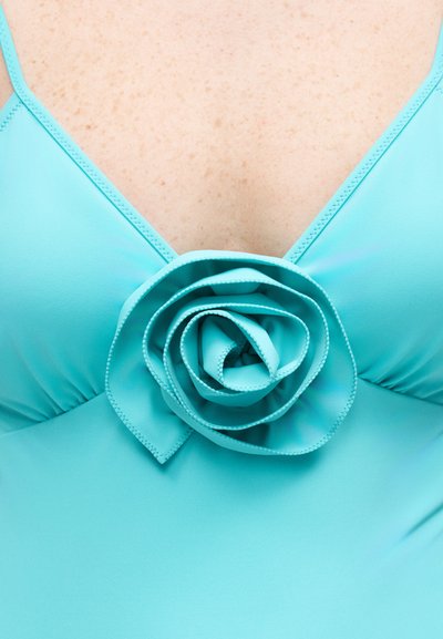 Κοντινό πλάνο ενός γαλάζιου μαγιό με βαθύ ντεκολτέ που διαθέτει μια μεγάλη υφασμάτινη ρόζα στο κέντρο.