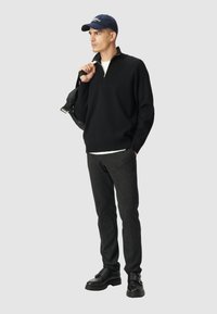 Maglione nero con zip, pantaloni grigi slim-fit e scarpe in pelle nera. Un berretto blu completa l'outfit. Design minimalista, senza motivi.