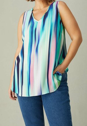 Kvinde iført ærmeløs, flerfarvet, stribet top i blå, turkis, pink og hvid, kombineret med blå jeans, hånd i lommen, beige baggrund.