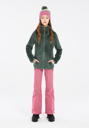 Fleecejacke in Grün mit hochgeschlossenem Kragen, Reißverschluss und seitlichen Taschen. Kombiniert mit pinkfarbenen wasserdichten Hosen und schwarzen Stiefeln.
