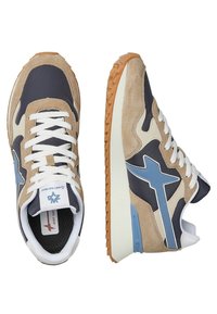 Sneaker beige e blu navy con materiali in suede e mesh, lacci bianchi, accenti blu e suola in gomma testurizzata. Presentano una sezione posteriore per l'ammortizzazione.