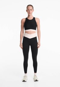 Fekete sportmelltartó fehér kivágással, fekete leggings-szel, amelyek krém színű chevron mintával rendelkeznek a derékrészen.