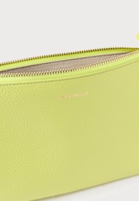 Zöld bőrből készült erszény texturált felülettel, aranyszínű cipzárral és a Coccinelle márkajelzéssel az elején. Kompakt és minimalista kialakítás.