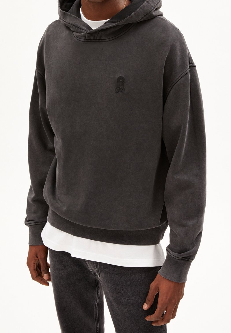 Tmavě šedá mikina s kapucí vyrobená z měkké tkaniny, která má vpředu klokaní kapsu a vyšívané logo na hrudi. Jednobarevná s volným střihem.